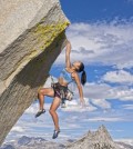 female rock climber struggles to reach her next grip as she battles her way up a steep cliff