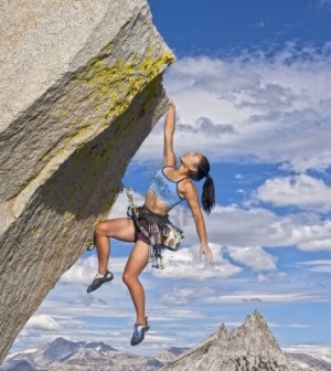 female rock climber struggles to reach her next grip as she battles her way up a steep cliff
